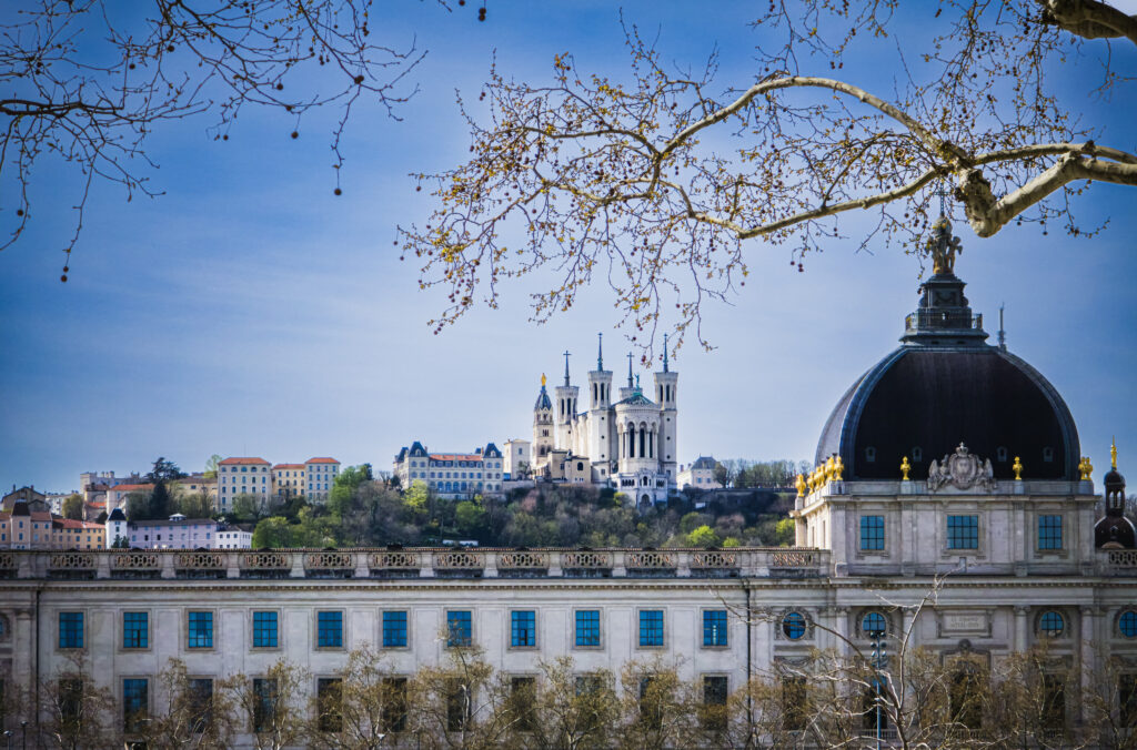 Grand Hôtel-Dieu w Lyonie z charakterystyczną kopułą oraz Bazylika Notre-Dame de Fourvière widoczna na wzgórzu w tle.