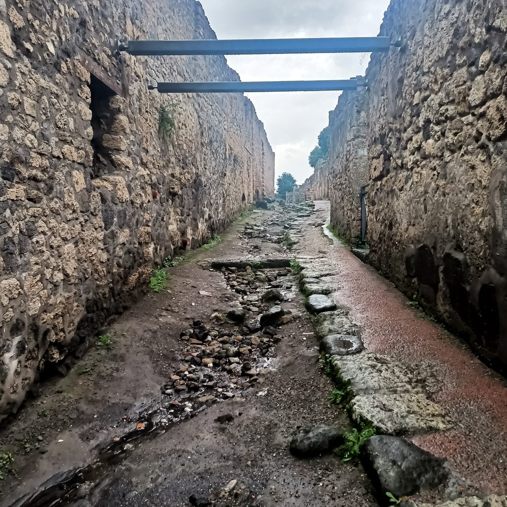 Wąska kamienna uliczka pomiędzy wysokimi murami starożytnych Pompejów po deszczu
