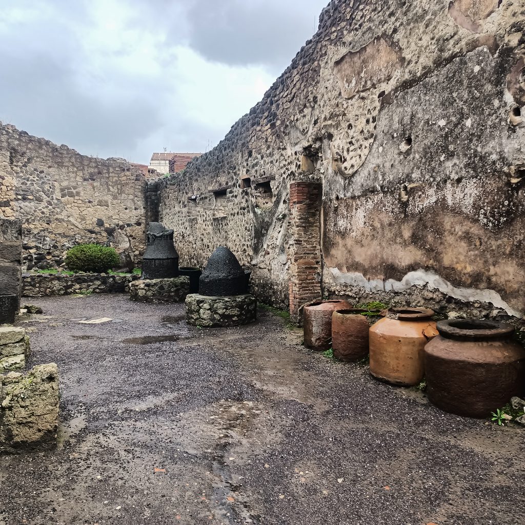Kamienne młyny do mielenia zboża i duże gliniane naczynia w dawnej piekarni w Pompejach