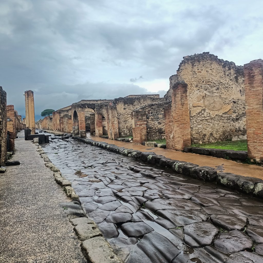 Mokra kamienna ulica w starożytnych Pompejach z ruinami domów po obu stronach