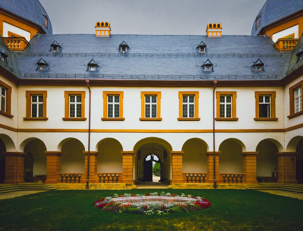Wewnętrzny dziedziniec pałacu Seehof w Memmelsdorfie z arkadami, centralnym przejściem i okrągłą rabatą kwiatow