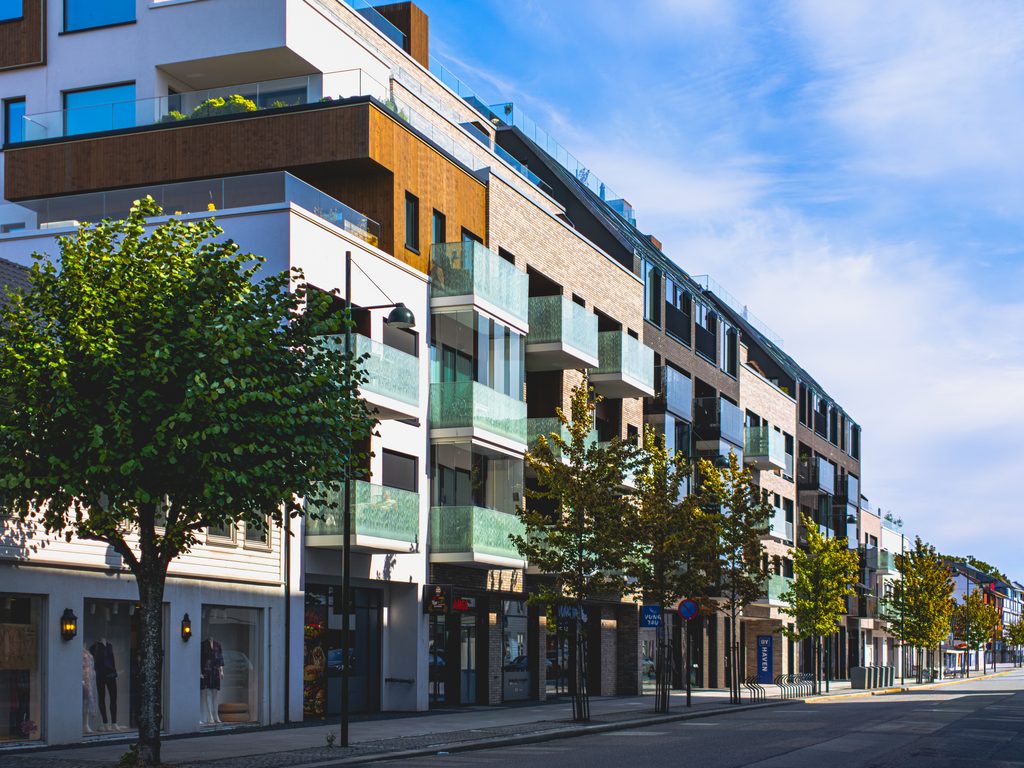 Nowoczesne budynki z przeszklonymi balkonami i drzewami wzdłuż ulicy w centrum Kristiansand, Norwegia.