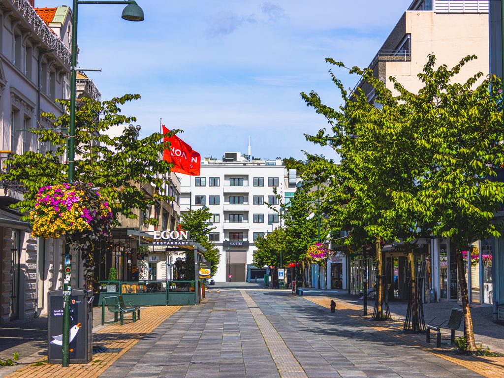 Deptak w centrum Kristiansand w Norwegii, z drzewami, kolorowymi kwiatami, restauracjami i zabytkowymi kamienicami.