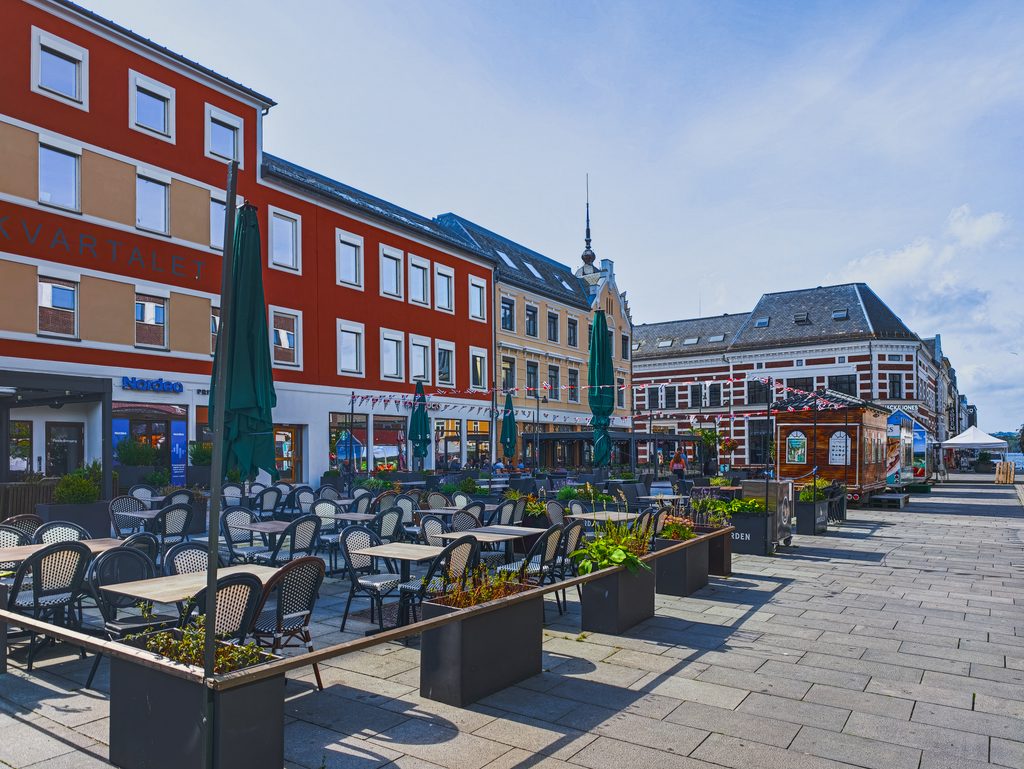 Ulica w centrum Kristiansand w Norwegii, z kolorowymi kamienicami, ogródkami restauracyjnymi i stolikami na świeżym powietrzu.
