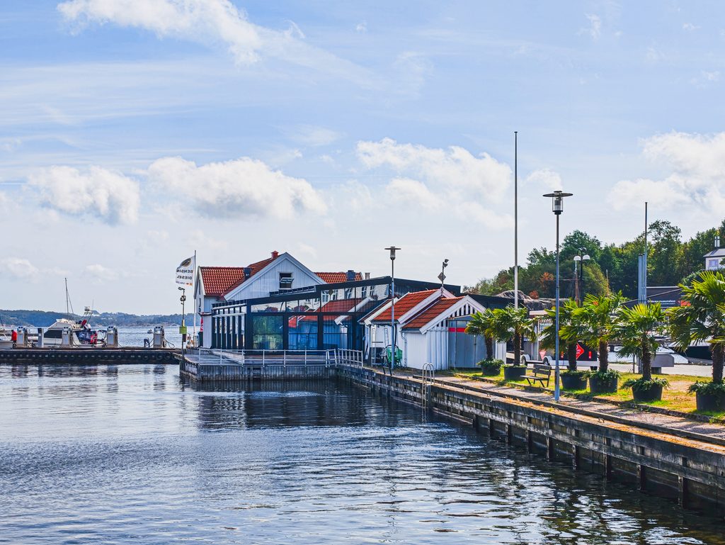Nabrzeże w Kristiansand z białymi drewnianymi budynkami, palmami i widokiem na port.